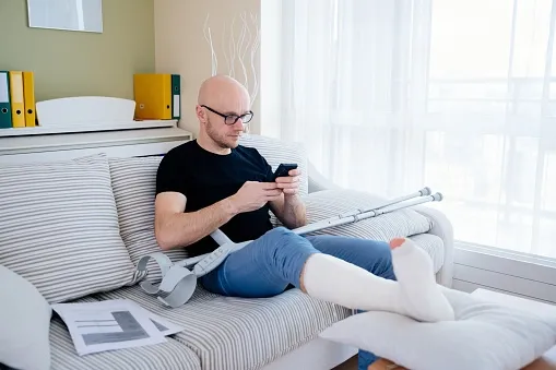 An person with a leg cast and crutches, sitting on a couch.
