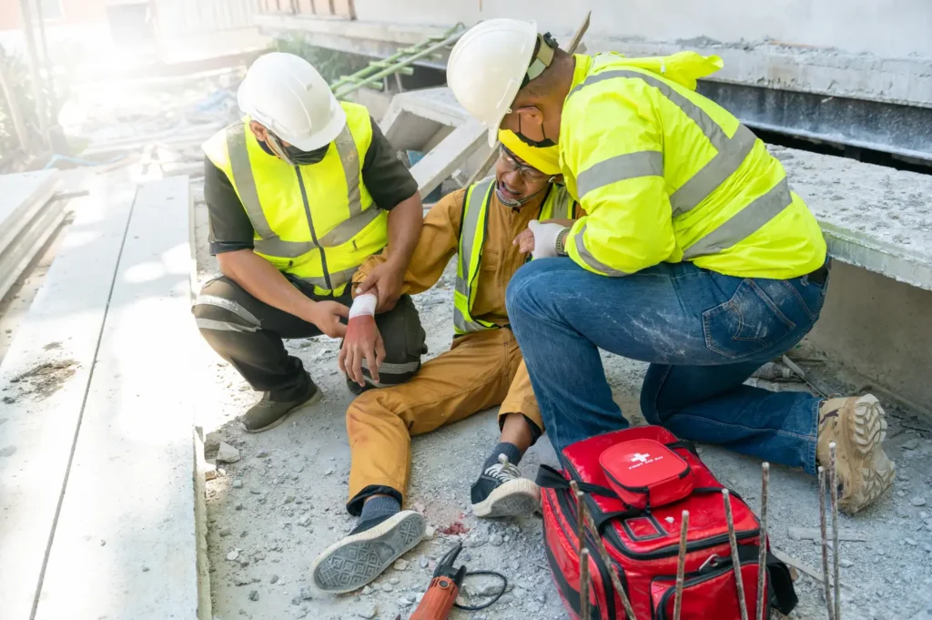An injured, in pain man at a construction site getting help from two other co-workers.